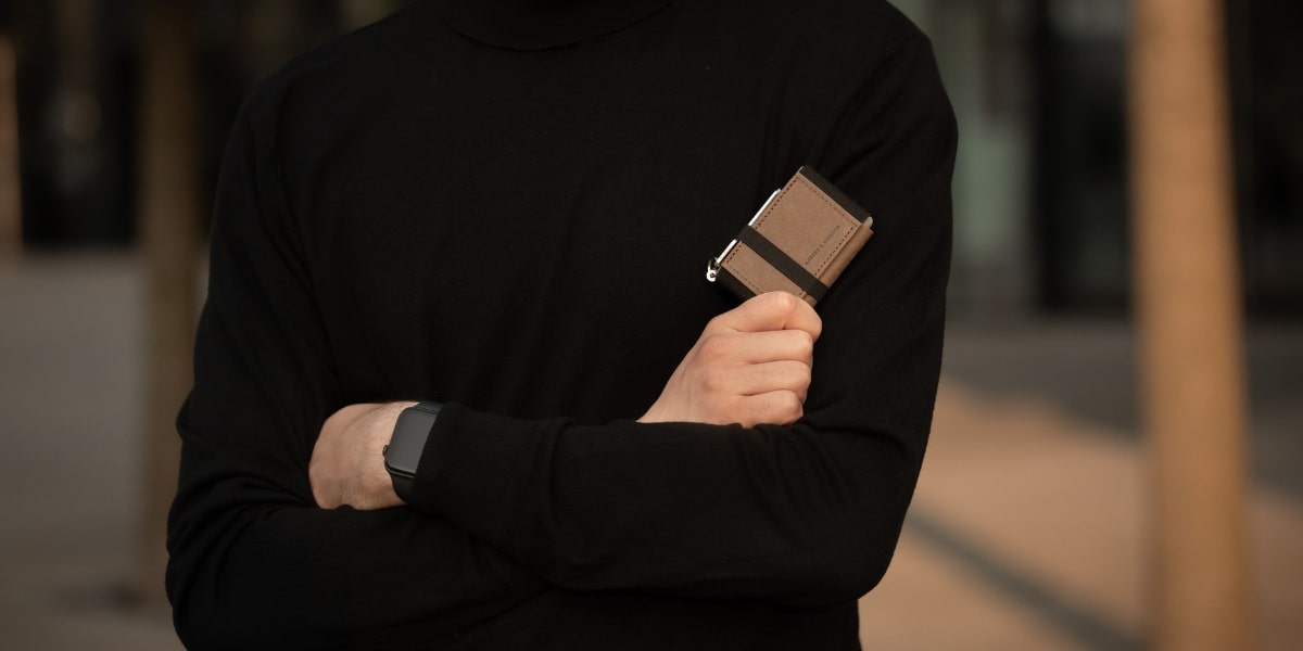 Card holder mit Münzfach in Braun/Schwarz in der Hand gehalten. Der Mann trägt einen schwarzen Rollkragenpullover.